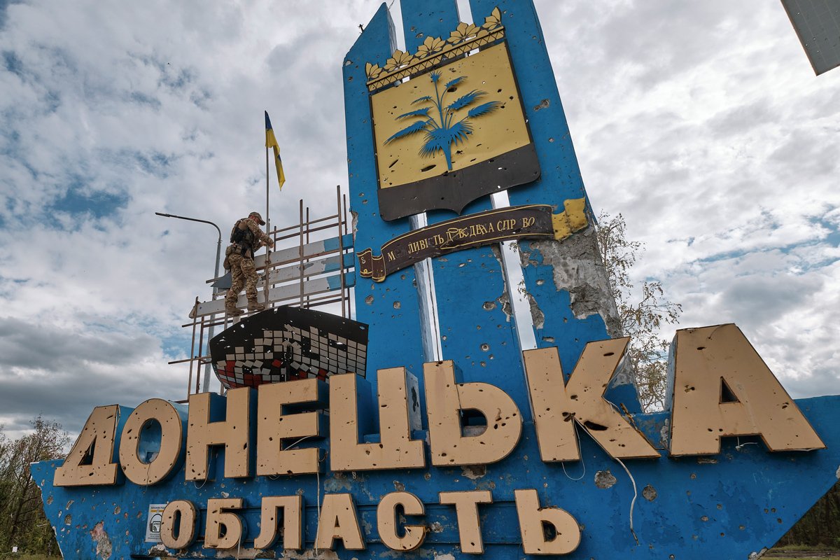 Военнослужащий поднимает украинский флаг над стелой на въезде в Донецкую область, Украина, 20 сентября 2022 года. Фото: Евгений Гончаренко / EPA-EFE