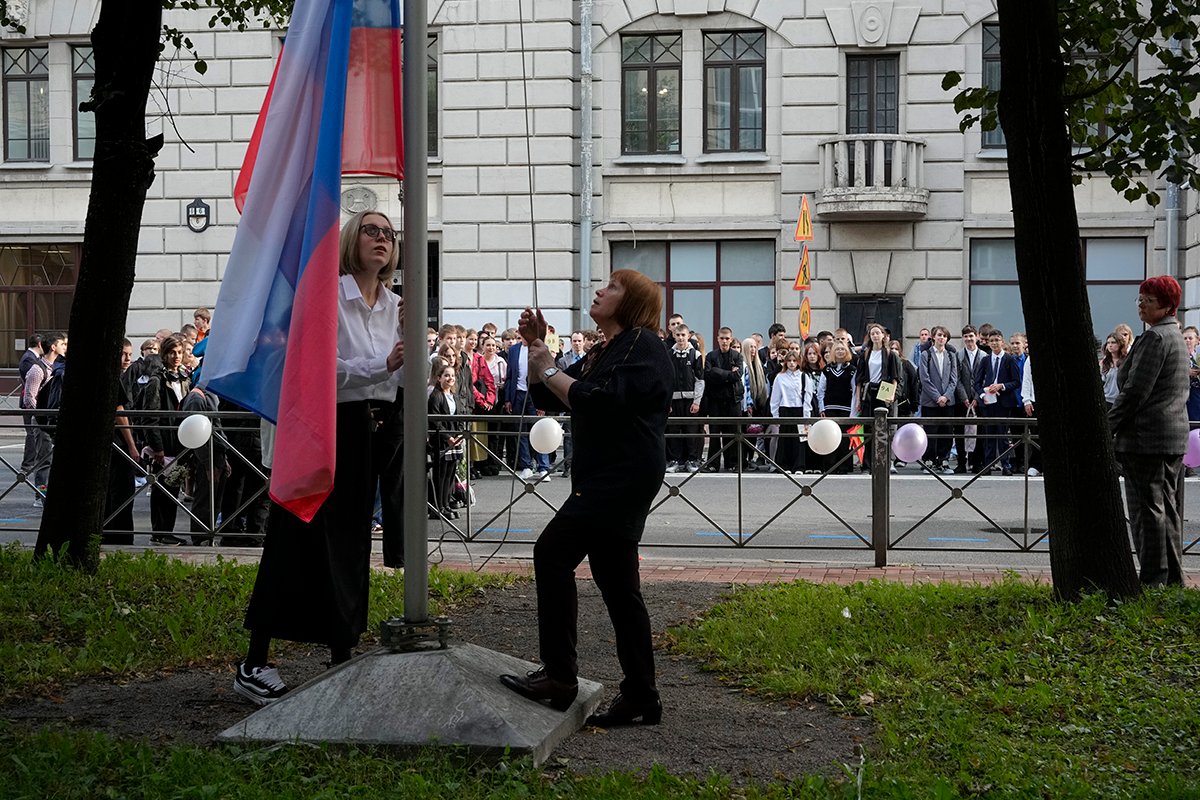 Учителя поднимают российский флаг во время церемонии, посвященной началу занятий в школе на «День знаний». Фото: Дмитрий Ловецкий / AP / Scanpix / LETA